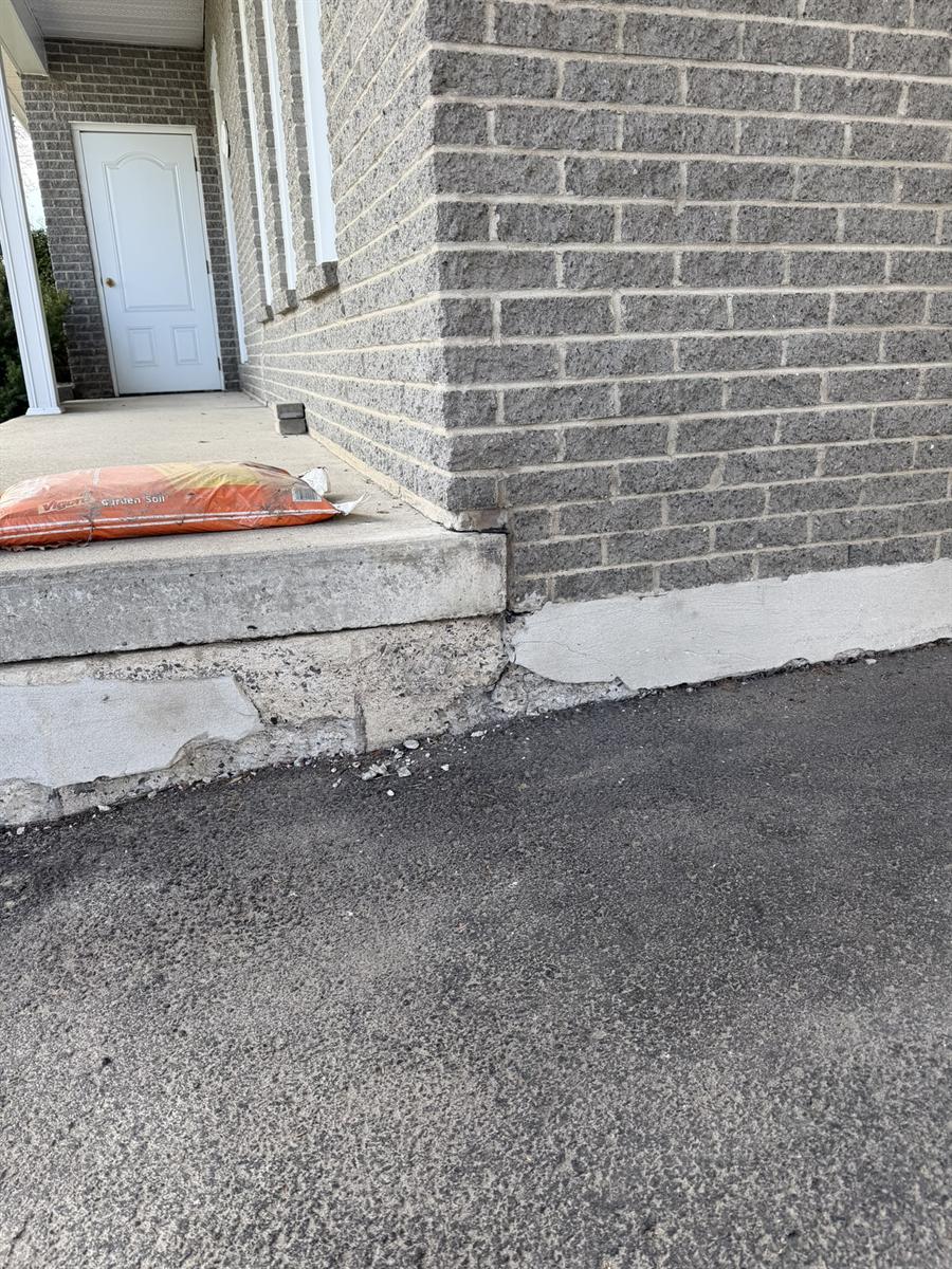 Bas de fondation en béton écaillé, agrégat exposé au pied d'un mur de brique