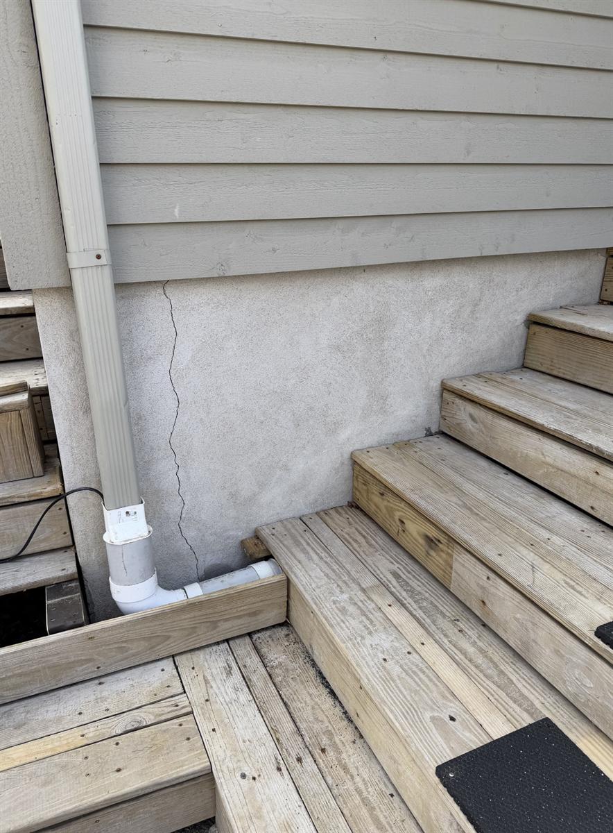 Fissure verticale dans un crépi de ciment au bas d'un mur, près d'un escalier