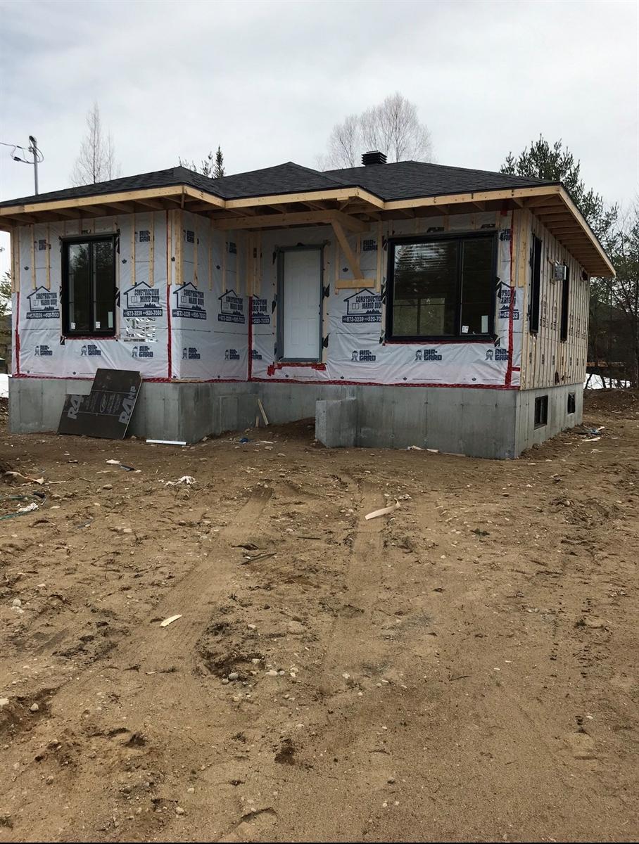 Maison neuve à l'étape du revêtement intermédiaire, fondation de béton apparente, avant la pose de la brique